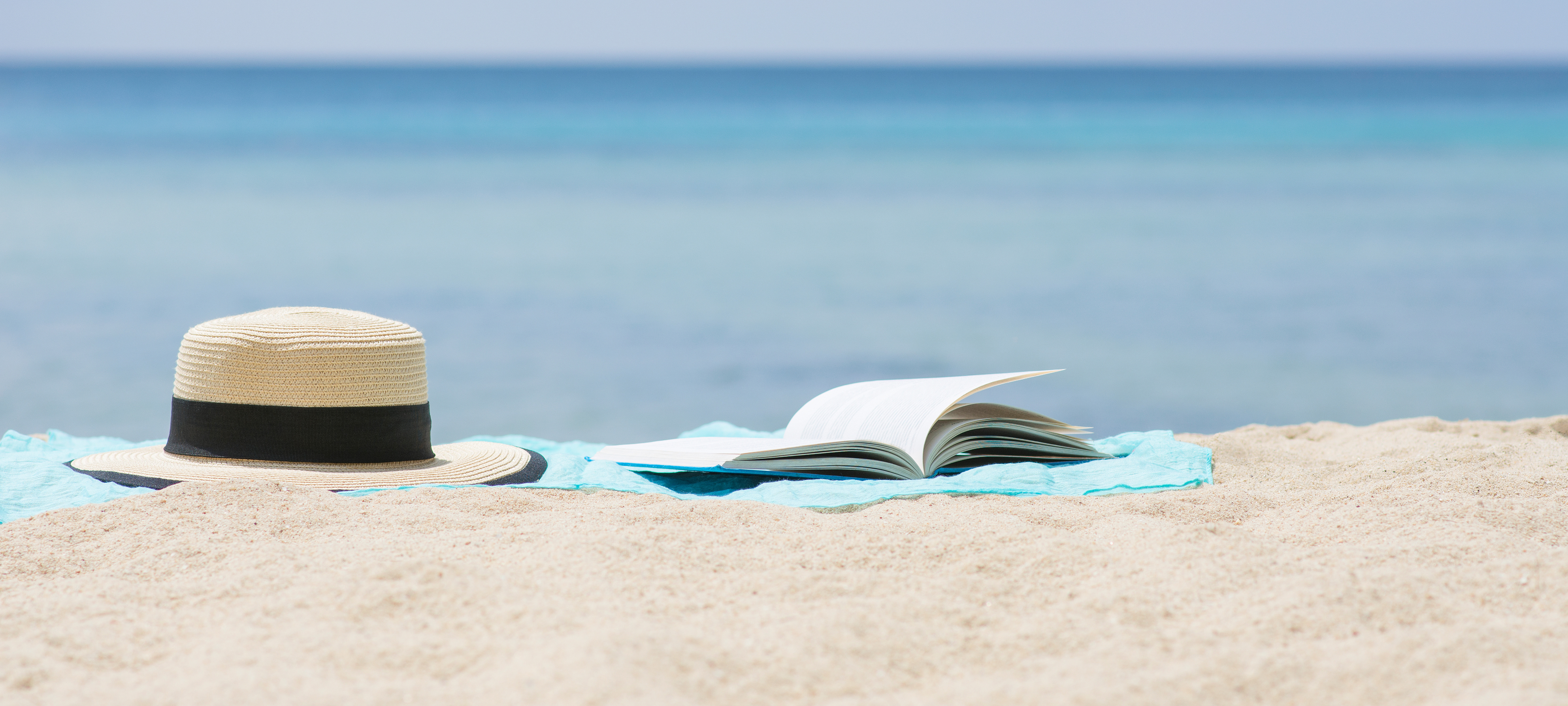 hat and open book on sandy beach