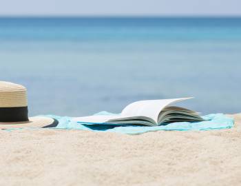 hat and open book on sandy beach