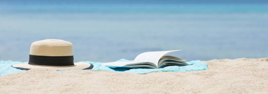 hat and open book on sandy beach